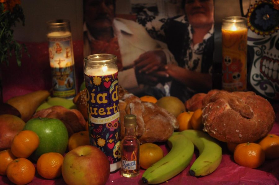 Traditional foods and drinks such as fruits, pan de muerto, and alcohol sit on an ofrenda.