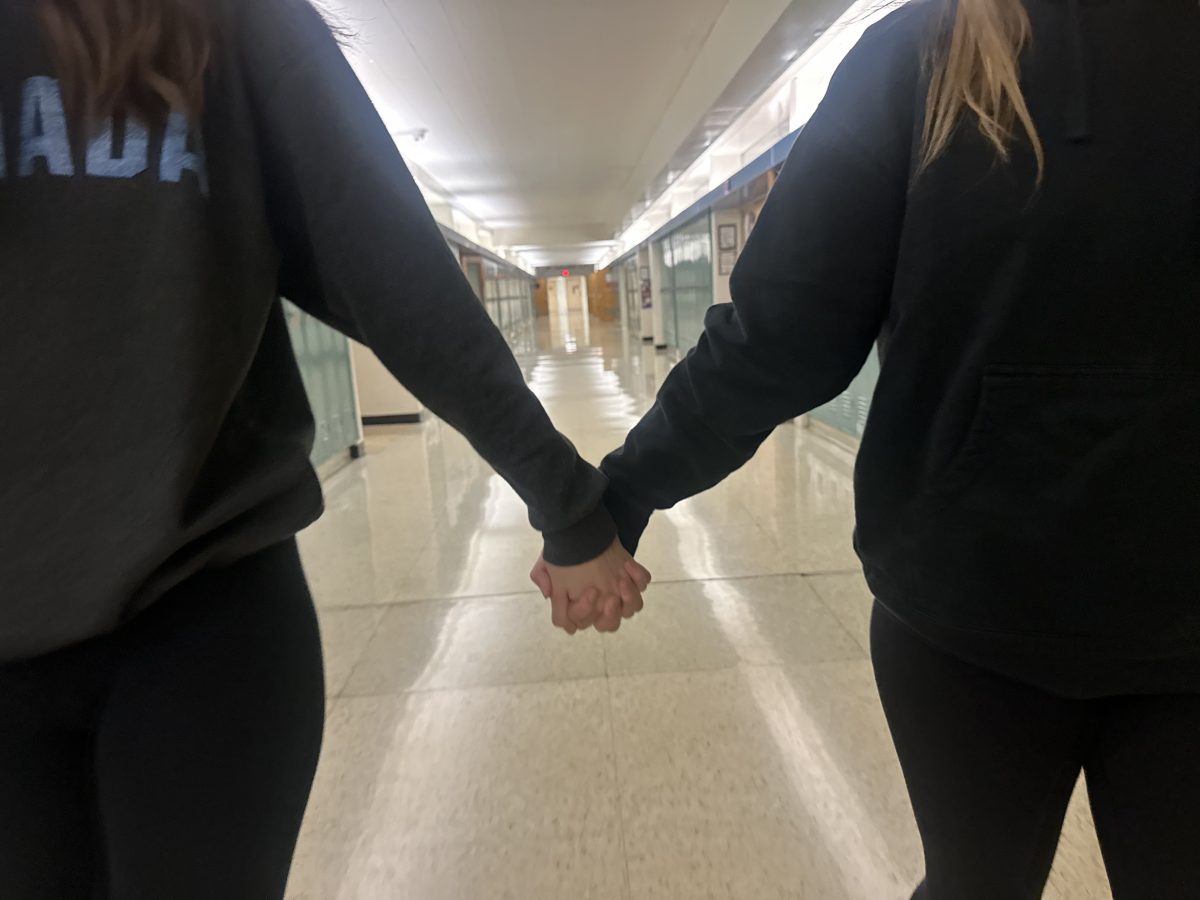 Two people holding  hands in the hallways of the school.