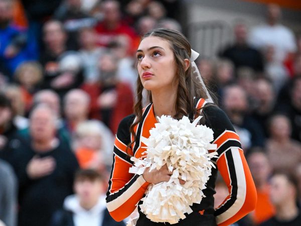 Senior Anna Woods stands for the National Anthem before the start of a boys' varsity basketball game.  